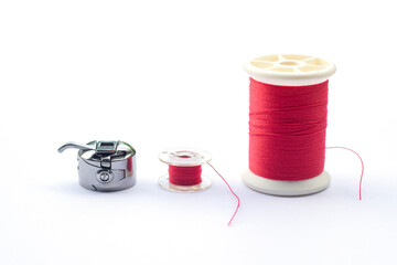 Red yarn and small bobbin is tools or parts of an electric sewing machine isolated on white background.