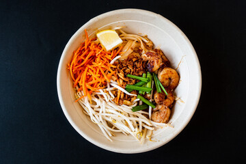 Asian dish Pad Thai prepared with noodles, grilled shrimps, soy sprouts, carrots pieces and sprinkle with peanuts to serve a delicious meal