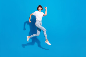 Fototapeta na wymiar Photo of pretty charming young woman dressed casual clothes jumping running fast smiling isolated blue color background