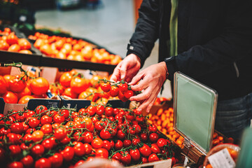 man hand holding cherry tomato in grocery store in supermarket