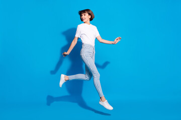 Photo of cute shiny young woman dressed casual clothes running looking back empty space smiling isolated blue color background