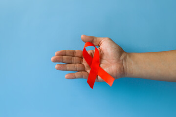 World Aids Day and World Diabetes Day with male hands holding red AIDS awareness ribbon isolated on blue background. Healthcare and medicine concept. 