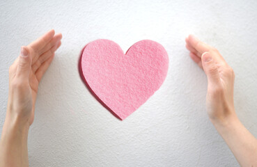 Hands surrounding a pink heart, symbol of love and care