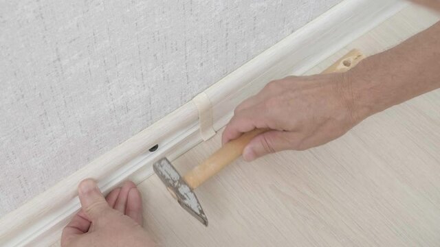 Professional repairman fixes light brown baseboard between floor and wall with special screwing gun during. man work on the installation of plastic plinth on wall. Room renovations at house