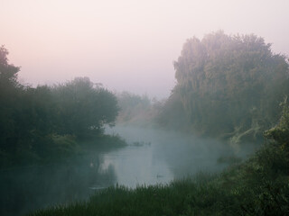 Fototapeta na wymiar Bend of a small river in heavy fog at dawn.