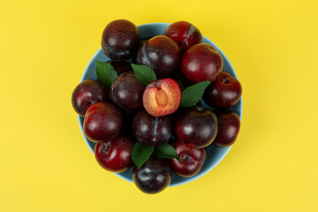 Blue bowl with plums on yellow background