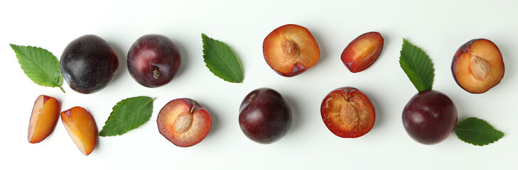 Tasty plums with leaves on white background
