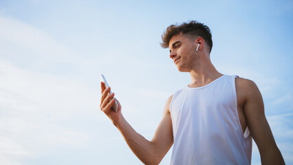 Sportsman with smartphone listening to song from earbud