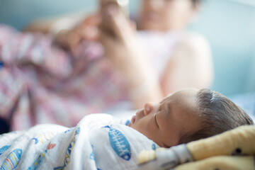 Baby boy sleep in home while mom using smartphone