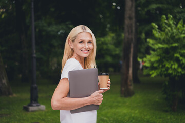Fototapeta premium Profile photo of aged funny blond lady hold laptop coffee wear white t-shirt in park alone