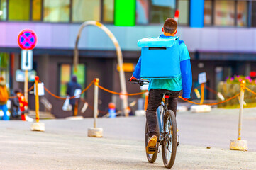 A young man working in a delivery service carries food to a customer in a backpack on a bicycle down the street. Fast and free food delivery by bike around the city.