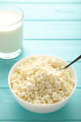 Cottage cheese and milk for breakfast in bowl on blue background. Vertical photo