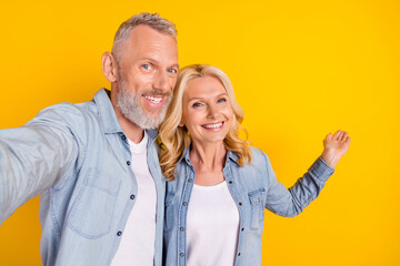 Photo of cheerful happy old couple spouses make selfie hand empty space isolated on yellow color background