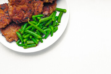 on a white background in a plate next to the cutlets lies green string beans; the choice between carcinogens in fried meat and the beneficial properties of legumes; the photo contains a copy space