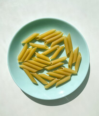 Raw penne Italian pasta on the blue plate on the white table.	
