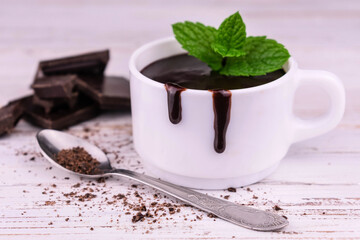 Hot chocolate in a cup with mint leaves on a white wooden background.
Close-up.