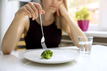 Poster dieting problems, eating disorder - unhappy woman looking at small broccoli portion on the plate © ronstik