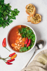Vegetarian bean soup with tomato, hot peppers and green parsley. Vegan stew with legumes and vegetables. White background, top view