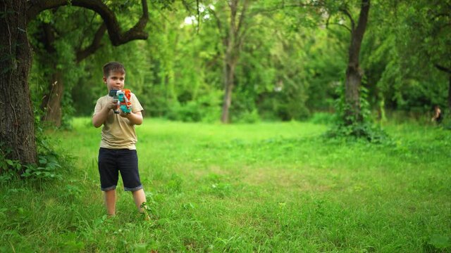 Child Holds Toy Gun and Shoots Cartridges. In Garden, Boy Laughs and Fires his Blaster. Kid is Playing Trendy Popular Blaster. Jule 2020. Kyiv, Ukraine. High quality 4k footage