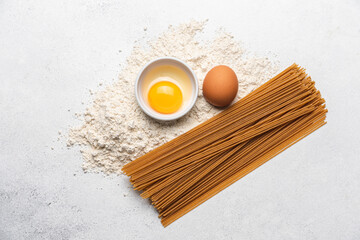 Ingredients for making whole grain pasta on light background. Integral brown spaghetti healthy alternative