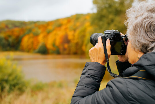 Retirement hobby, seniors and technology concept. Back view senior woman photographer uses digital camera, senior woman takes photo of autumn landscape outdoors, copy space. Selective focus on camera