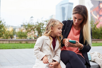 happy mom and her daughter are watching videos on smartphone