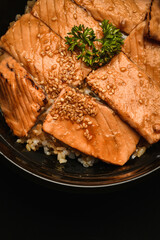 Salmon on rice looks appetizing in a black bowl.