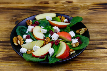 Autumn spinach salad with apple, feta cheese, walnut and dried cranberry on wooden table. Healthy vegetarian food