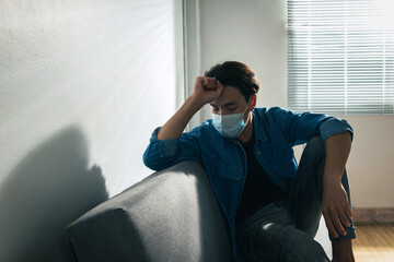 Fototapeta premium An upset health problem Asian patient man wearing a face mask at home or hospital alone sad and waiting for a doctor. Hospital and Health care during Coronavirus or Covid-19 quarantine concept