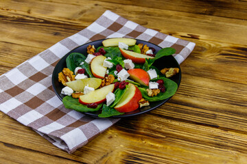 Autumn spinach salad with apple, feta cheese, walnut and dried cranberry on wooden table. Healthy vegetarian food