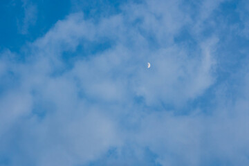 Half moon on blue bright sky background and clear clouds on daytime