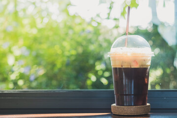 Side view of iced dark cold brew americano coffee on the plastic cup and brown plastic straw on the wooden bar table with copy space in coffee shop.