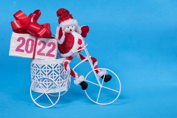 2022 text on gift box with red ribborn and santa claus toy on bicycle. Blue background. Christmas...
