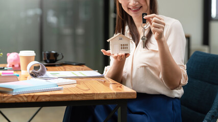 Young businesswoman holding a house model with key to deliver a client at office.