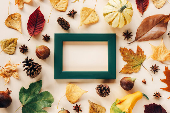 Blank picture frame and autumn leaves, pumpkins, figs and cones on light beige background. Mock up, top view, copy space