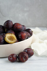 On a gray background, a blurred image of plums in a beige ceramic plate.