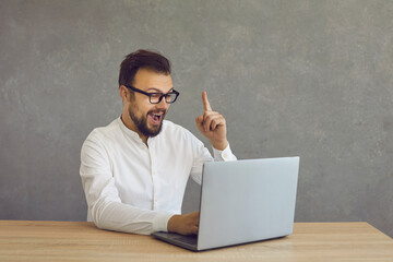 Aha. Eureka. Cheerful hipster man sitting at laptop computer has brilliant idea, gets sudden...