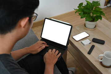 Behind shot of a young smart man is typing on a white blank screen digital tablet with a keyboard...