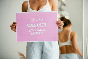 Close-up of woman holds pink breast cancer awareness month sign.