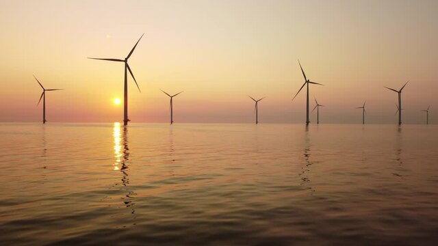 Wind turbines producing sustainable renewable energy in an offshore wind park during sunset. Drone point of view.
