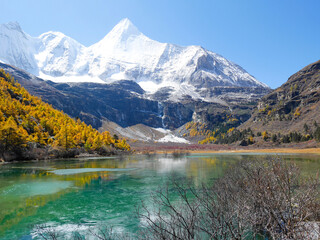 View of snow covered mountain peaks, autumn leaves and green lake