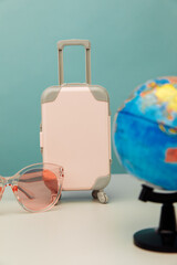 Travel concept. Plastic travel suitcase, pink glasses and globe. Vertical image