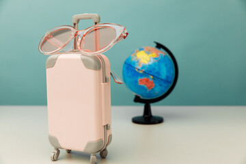 Plastic travel luggage, pink glasses and globe on a table. Traveling concept