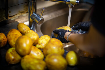hands with black plastic gloves washing potatoes under the faucet