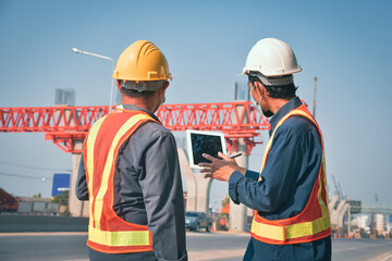 Two male construction engineers work at an elevated route construction site.