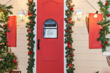 Christmas porch decoration idea. House entrance with red door decorated for holidays. Red and green...