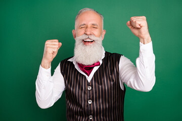 Photo of excited cheerful senior well-groomed man raise fists wear striped suit on green color background