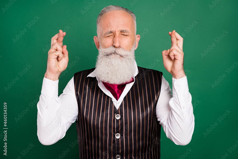 Sticker Photo of nervous well-groomed mature man hold crossed fingers beg wish wear striped waistcoat on green color background