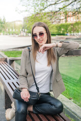 Beautiful fashion stylish woman with eyeglasses sitting on the bench in the city