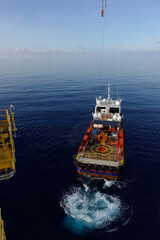 Cargo being loaded from a oil and gas platform onto a supply vessel and vessel crew give hand...